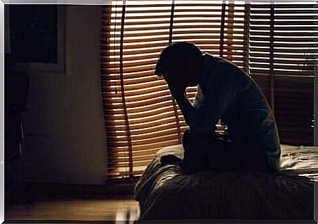 Man sitting on the bed in the dark.