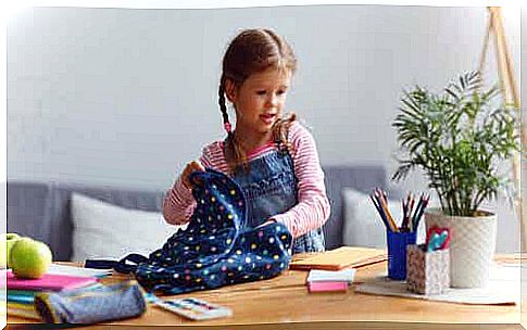 Little girl taking notebooks from backpack.